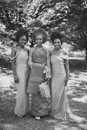 Black and white photo of three women in formal attire with traditional gele headwraps and elegant dresses.