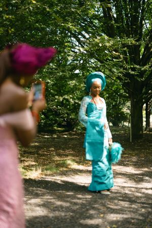 A group takes photos outdoors of someone in a turquoise traditional dress and headwrap.