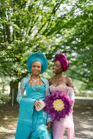 Two women in elegant traditional dress pose together outdoors with pink and turquoise outfits.