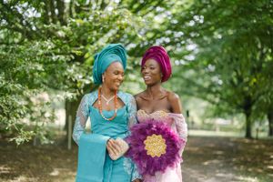 Two wedding attendees share a joyful moment while holding a purple floral bouquet outdoors.