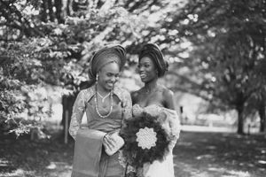 A black and white photo captures two wedding attendees sharing a candid moment outdoors.