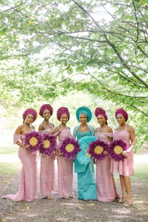 Wedding party members pose together holding purple sunflower bouquets in coordinated pink and turquoise attire.