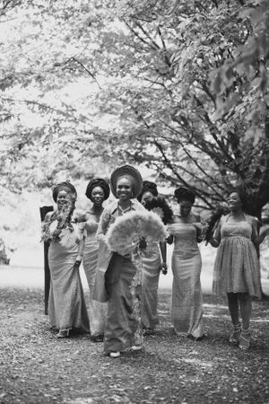 A vintage black and white photo of a wedding party posing with fans under trees.