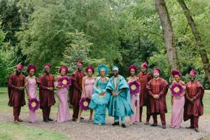 Large wedding party wearing pink, burgundy and turquoise traditional attire poses outdoors.