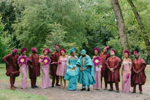 Wedding group in coordinated cultural attire of pink, burgundy and turquoise gather in garden setting.