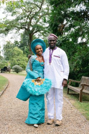 Couple in traditional turquoise and white attire pose together on garden path.