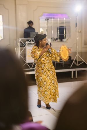Performer in a golden patterned dress singing on stage with purple lighting.