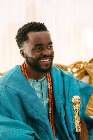 Guest wearing traditional teal agbada with orange beaded necklace at cultural celebration.