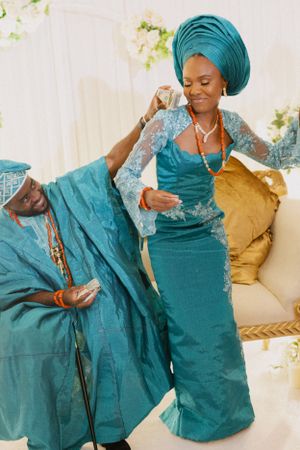 Couple in matching teal traditional attire sharing joyful moment on couch.