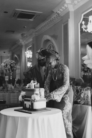 Black and white photo of couple cutting their wedding cake at reception.