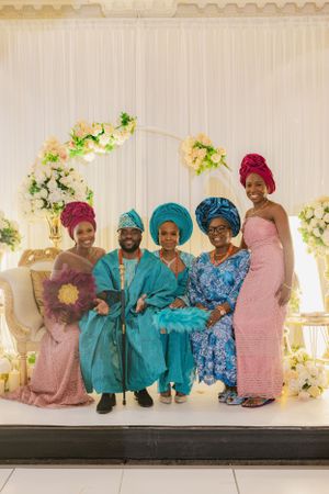 Group photo of wedding party in traditional African attire with pink and teal color scheme.