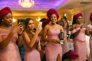 Bridesmaids in matching pink dresses and red headwraps using phones during wedding reception.