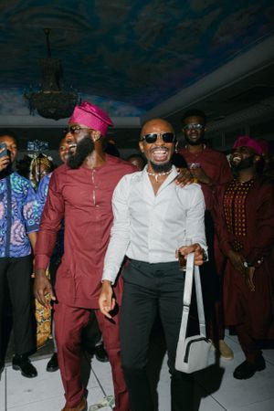 Wedding guests in traditional African formal wear including burgundy agbada and modern suits.