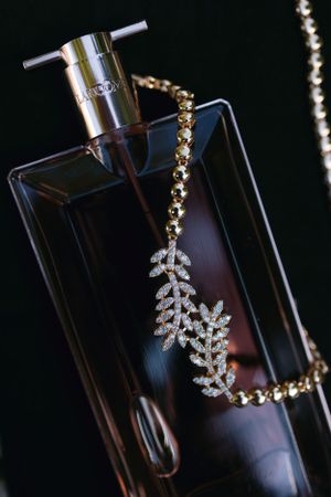 Elegant diamond leaf pendant necklace displayed against a perfume bottle in dark lighting.