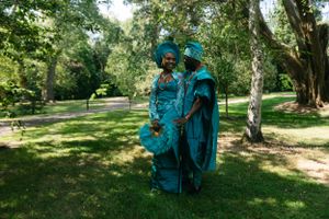 Couple in matching turquoise traditional outfits pose in sunny garden setting.