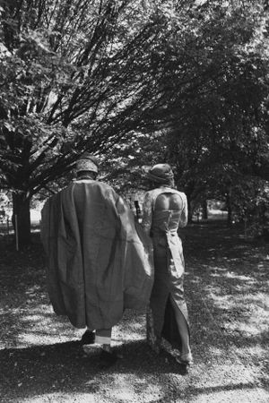 Black and white photo of two people walking down a tree-lined path.