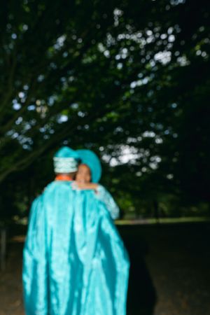 A blurred photo of two people wearing matching turquoise traditional attire embracing outdoors.