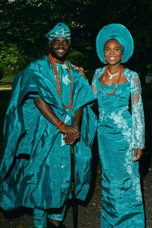 Two people in elegant turquoise traditional Nigerian attire pose together outdoors.