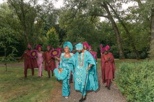 Wedding party members in burgundy and turquoise outfits walk along an outdoor garden path.