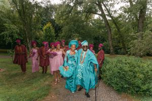 A wedding party in vibrant turquoise and burgundy attire walks along a garden path.