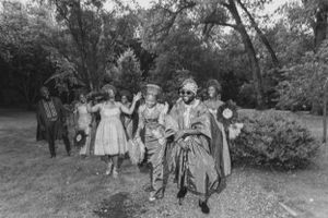 A vintage black and white photograph of a wedding party walking through a garden setting.