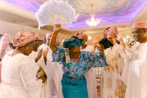 Dancers in traditional white and blue attire celebrate beneath a chandelier at a formal event.