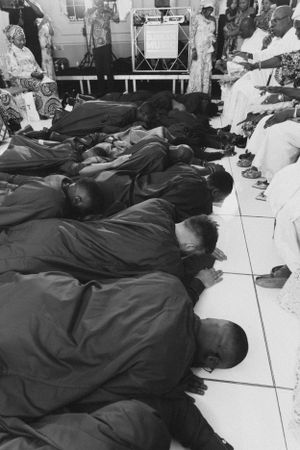 A black and white image shows people prostrating during a traditional religious ceremony.