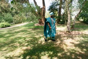 Person wearing vibrant turquoise traditional attire standing in a sunny garden setting.