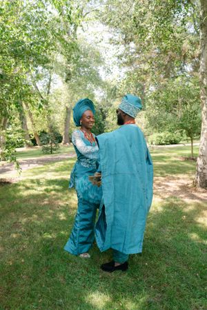 Couple in coordinated turquoise formal wear interact in a sunlit garden.