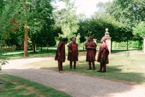 Four people in burgundy ceremonial robes stand on a garden path.