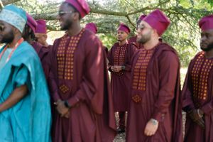 Row of people in matching burgundy robes and magenta caps at outdoor ceremony.