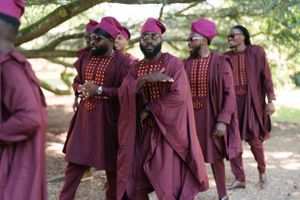 Group wearing burgundy robes and magenta caps congregate during outdoor ceremony.
