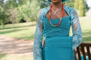 Close-up of turquoise dress with lace sleeves and coral beaded necklace.
