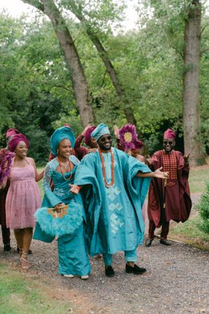 Wedding celebration with guests in colorful Nigerian attire dancing together on a wooded path.