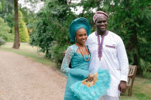 Couple in traditional West African wedding attire walking together on a garden path.