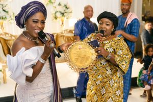 Two performers in elegant African attire sing and entertain at a formal celebration.
