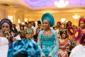 Attendees in vibrant traditional dress gather under chandeliers at a formal celebration.