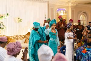 Crowd celebrates in coordinated turquoise and pink traditional outfits at an indoor event.
