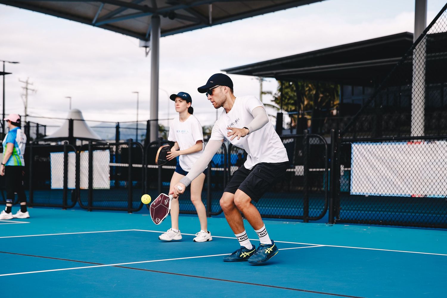 A tennis player wearing blue athletic wear hits a backhand shot on an outdoor tennis court.