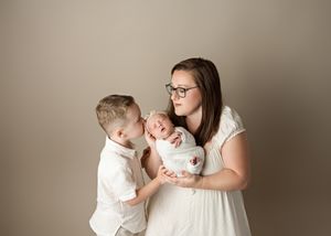 Siblings tenderly looking at newborn baby against neutral beige background in studio portrait setting.