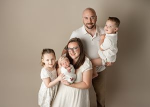 A family dressed in white poses together against a neutral backdrop for a professional studio portrait.