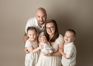 A family wearing white poses together for a studio portrait against a neutral beige background.
