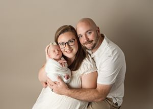 A happy family dressed in white embraces warmly together against a neutral beige studio backdrop.