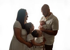 A family wearing coordinated beige and white outfits shares a tender moment together against a light background.