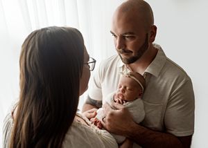 Parents share a tender moment with their newborn baby in a soft natural light setting.