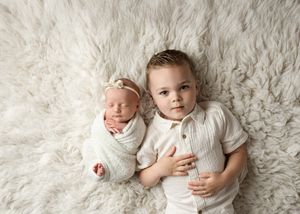 Two siblings in white outfits pose together on a cozy white fur background for a heartwarming portrait.
