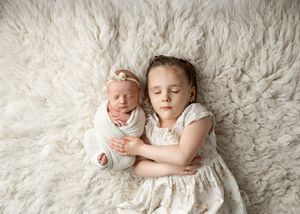 Two children peacefully sleeping together on a plush white fur rug, wearing light-colored clothing.