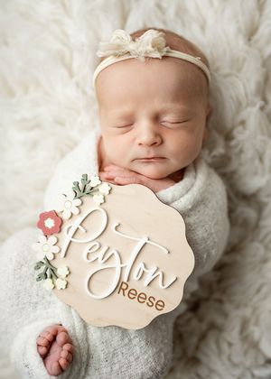 Newborn sleeping peacefully on white fluffy rug with delicate headband and decorative name plaque reading Peyton Reese.