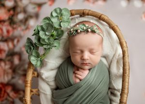 Peaceful sleeping baby wrapped in sage green swaddle with floral crown in rustic basket with eucalyptus decor.