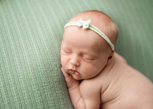 Close-up of sleeping newborn on mint green fabric wearing simple white bow headband.